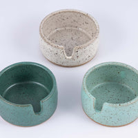 Closer view of three stoneware ashtrays each a different color of speckled clay- white, light blue, and darker greenish blue