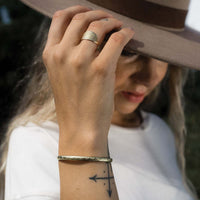 Woman's hand grabbing the side of her felt hat while wearing a brass sunburst ring and brass bracelet