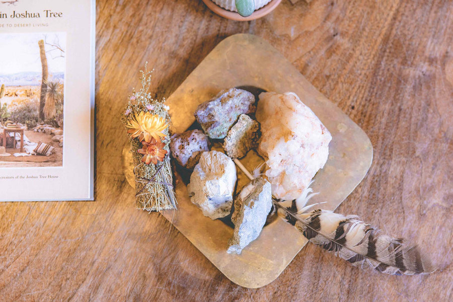 A white sage bundle decorated with desert flowers on top of a burner with rocks and large bird feather