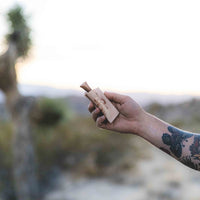 Man's arm holding a tan leather sheath with golden sidewinder snake design encasing a wood handle pocket knife